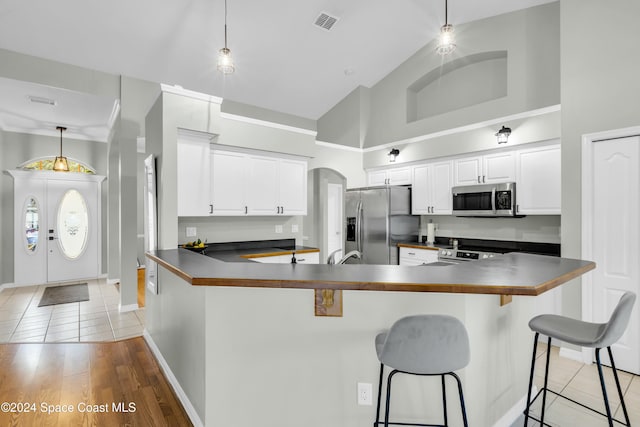 kitchen with light hardwood / wood-style flooring, white cabinets, decorative light fixtures, and appliances with stainless steel finishes