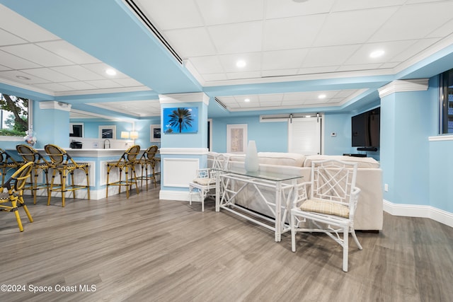 interior space with a drop ceiling, light hardwood / wood-style floors, a barn door, and crown molding