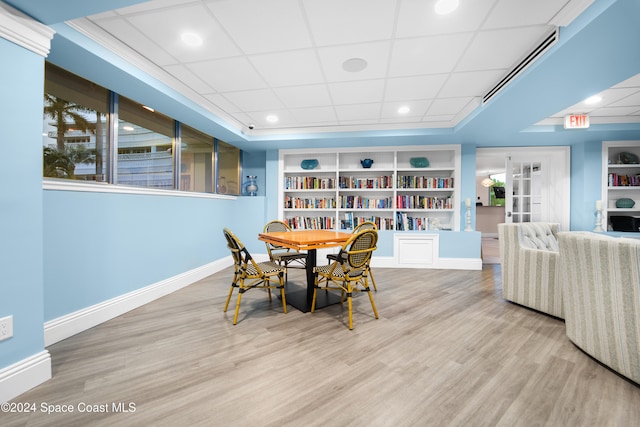 dining room with light hardwood / wood-style floors, built in features, and a drop ceiling