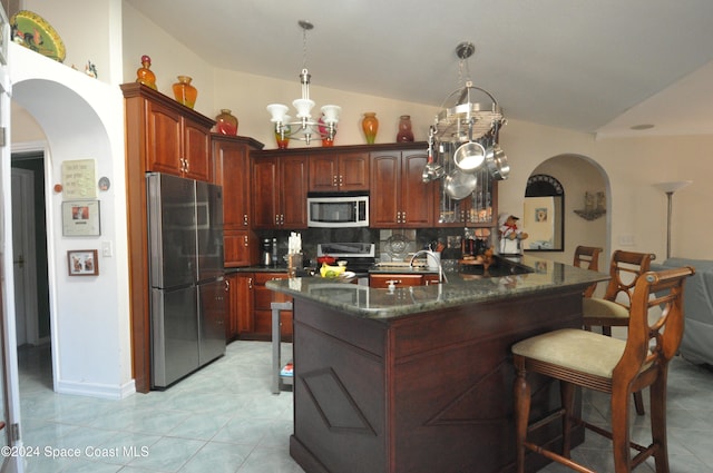 kitchen with lofted ceiling, a kitchen island with sink, backsplash, appliances with stainless steel finishes, and decorative light fixtures