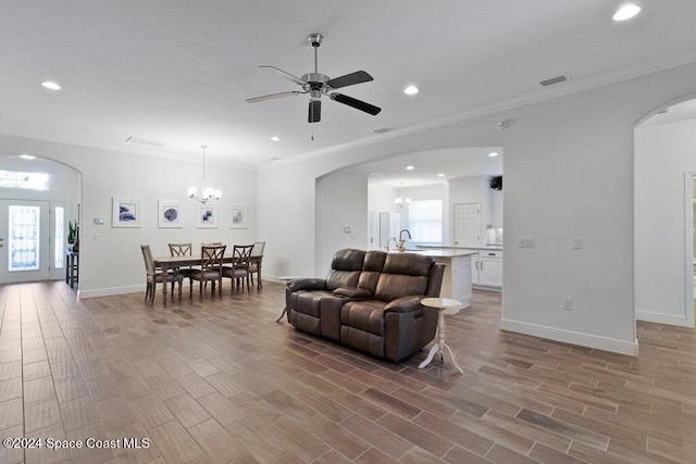 living room with sink, ornamental molding, ceiling fan with notable chandelier, and light wood-type flooring