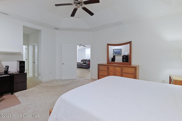 bedroom with light colored carpet, a raised ceiling, and ceiling fan