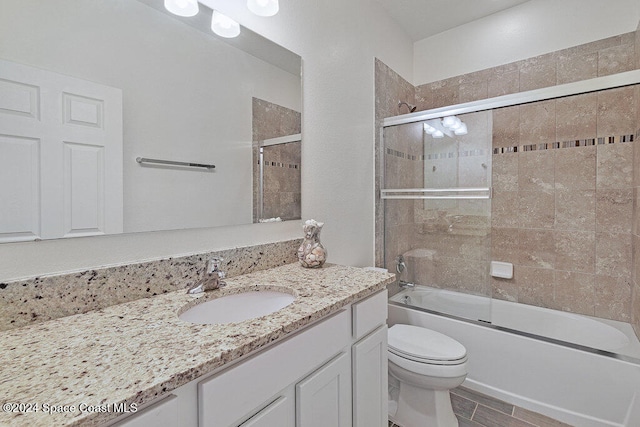 full bathroom with hardwood / wood-style floors, toilet, combined bath / shower with glass door, and vanity