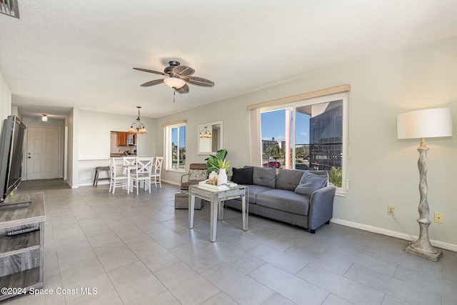 living room featuring a textured ceiling, light tile patterned flooring, and ceiling fan with notable chandelier