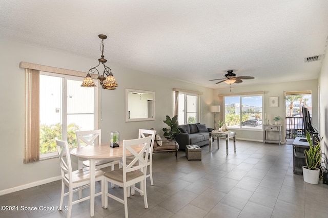 tiled dining area featuring a textured ceiling and ceiling fan with notable chandelier