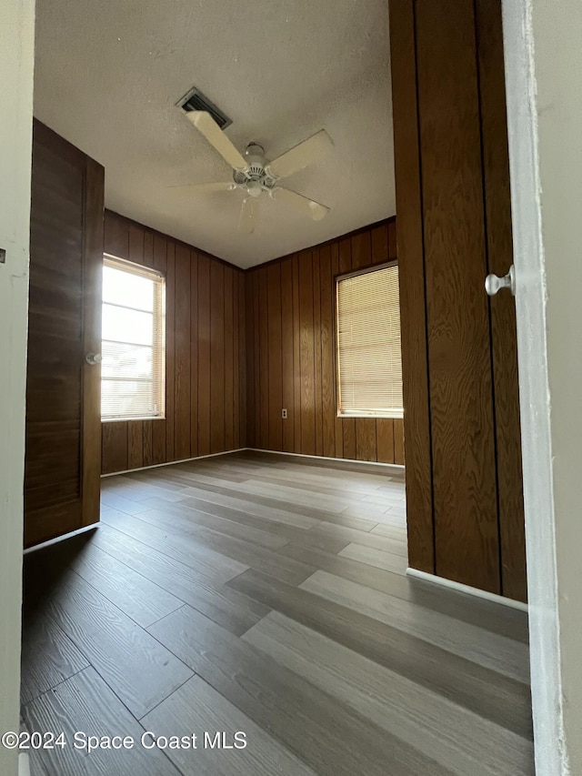 empty room with ceiling fan, wooden walls, a textured ceiling, and light wood-type flooring