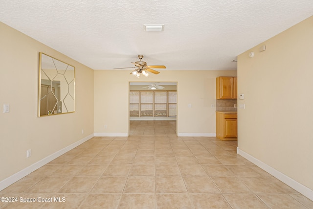 empty room with ceiling fan, light tile patterned floors, and a textured ceiling