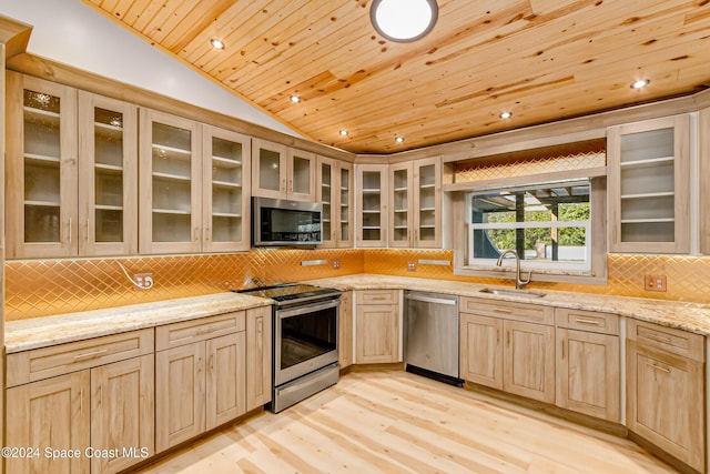 kitchen with lofted ceiling, light brown cabinetry, sink, stainless steel appliances, and light stone countertops