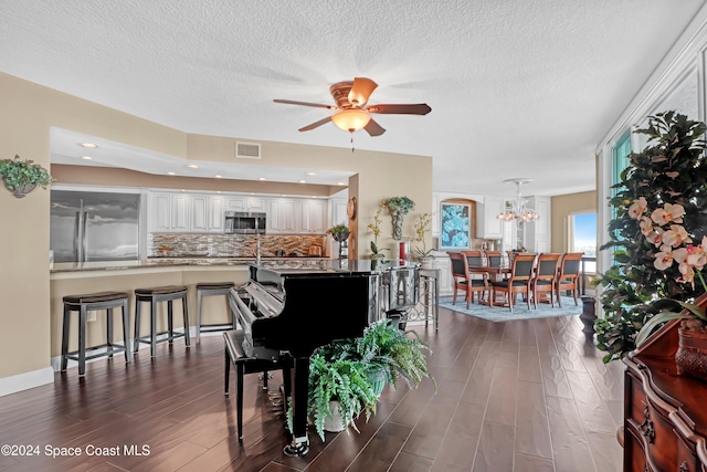 interior space featuring a textured ceiling, ceiling fan with notable chandelier, and dark wood-type flooring