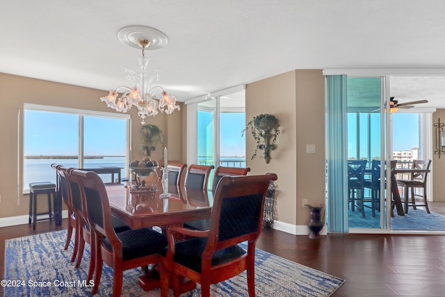 dining area featuring ceiling fan with notable chandelier, a water view, and dark wood-type flooring