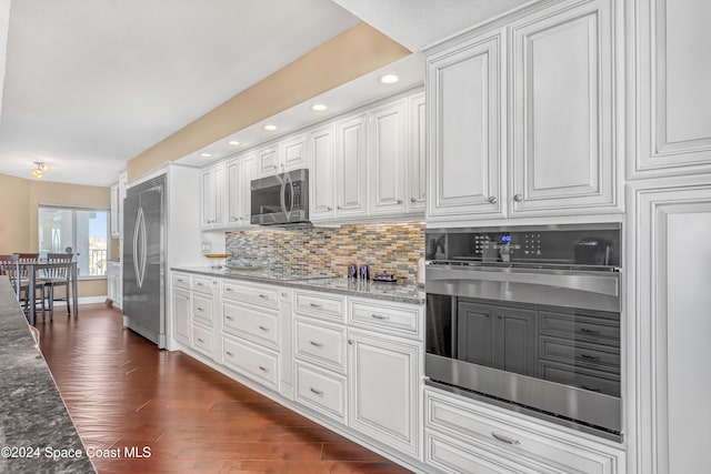 kitchen featuring dark hardwood / wood-style flooring, tasteful backsplash, stainless steel appliances, stone countertops, and white cabinetry