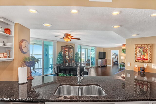 kitchen with a textured ceiling, ceiling fan, dark stone counters, and sink