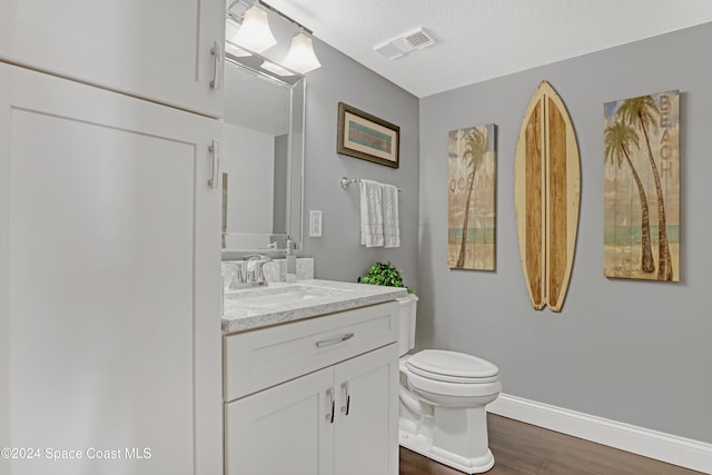 bathroom with hardwood / wood-style floors, vanity, toilet, and a textured ceiling