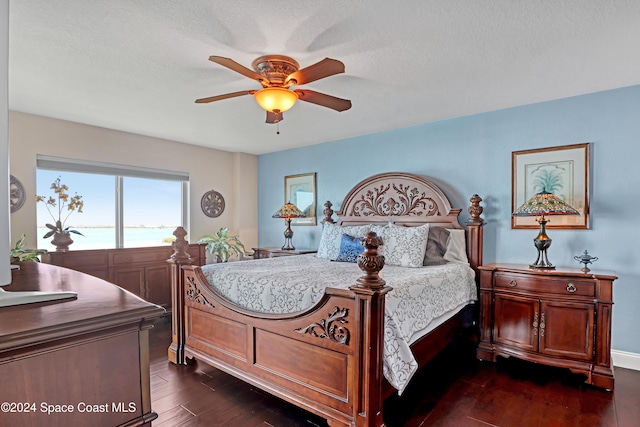 bedroom featuring ceiling fan, dark hardwood / wood-style flooring, a water view, and a textured ceiling