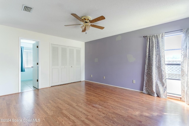 unfurnished bedroom with ceiling fan, a closet, multiple windows, and light hardwood / wood-style flooring