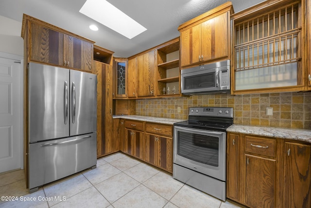 kitchen with a skylight, light stone countertops, backsplash, light tile patterned floors, and appliances with stainless steel finishes