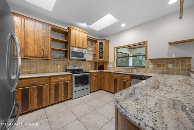 kitchen featuring a skylight, light stone countertops, sink, and stainless steel appliances