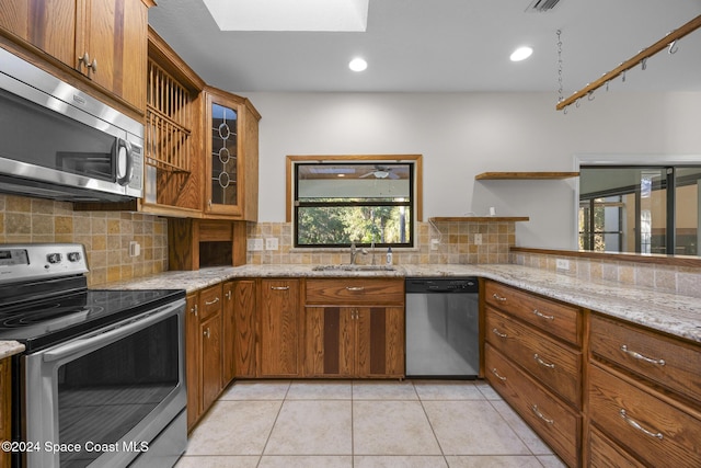 kitchen with a skylight, light stone counters, sink, and appliances with stainless steel finishes