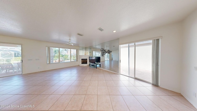 unfurnished living room with ceiling fan, light tile patterned flooring, and a textured ceiling