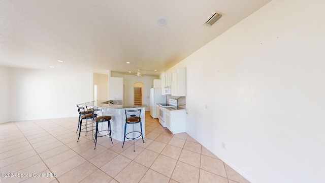 kitchen featuring white cabinets, kitchen peninsula, white appliances, a kitchen bar, and light tile patterned floors