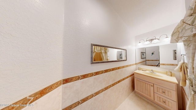 bathroom featuring vaulted ceiling, vanity, and tile walls