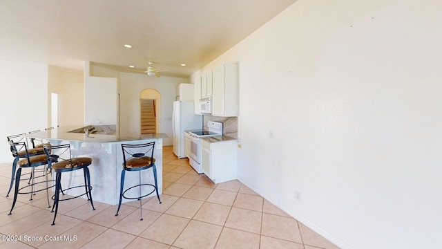 kitchen featuring kitchen peninsula, a kitchen breakfast bar, white appliances, ceiling fan, and white cabinets