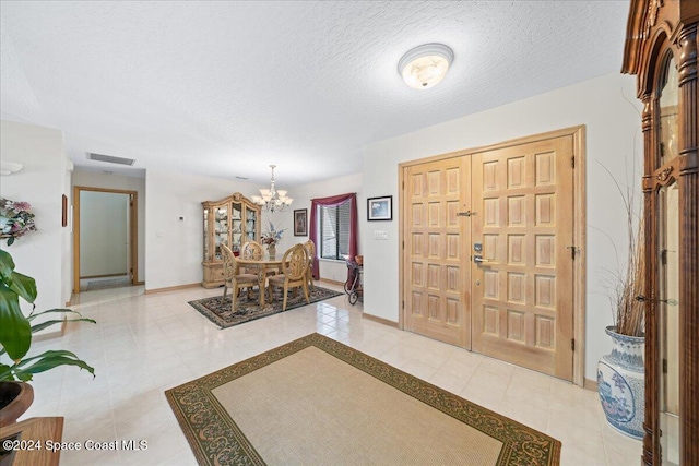 foyer entrance featuring light tile patterned floors, a textured ceiling, and a notable chandelier