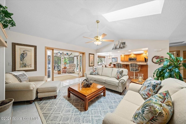 living room featuring light tile patterned floors, a textured ceiling, ceiling fan, and vaulted ceiling with skylight