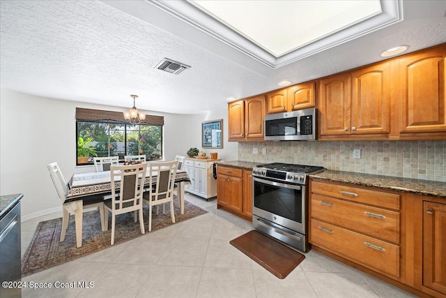 kitchen with a textured ceiling, backsplash, appliances with stainless steel finishes, and an inviting chandelier