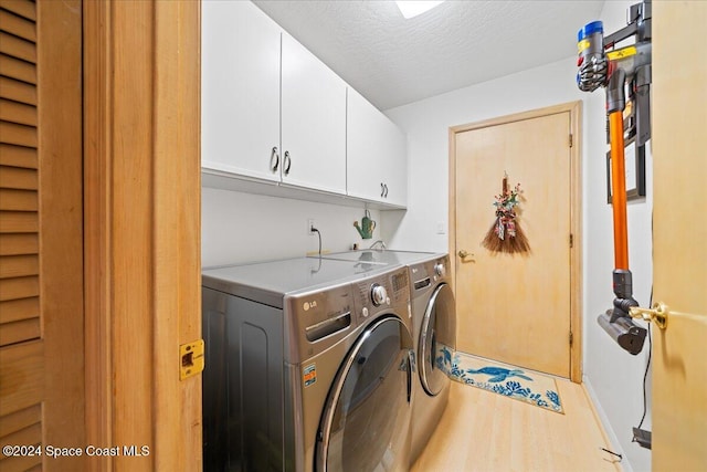 washroom featuring cabinets, a textured ceiling, separate washer and dryer, and light hardwood / wood-style floors