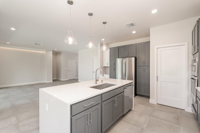 kitchen with appliances with stainless steel finishes, sink, pendant lighting, gray cabinets, and an island with sink