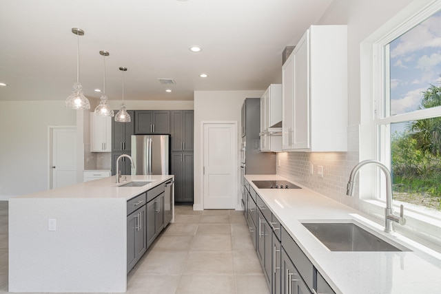 kitchen with gray cabinets, stainless steel appliances, a center island with sink, and sink