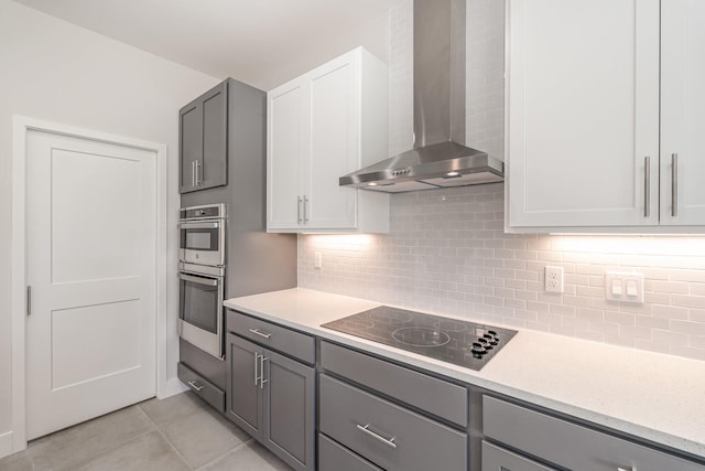 kitchen with backsplash, wall chimney exhaust hood, gray cabinets, black electric cooktop, and light tile patterned floors