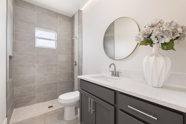 bathroom with tile patterned flooring, a tile shower, vanity, and toilet