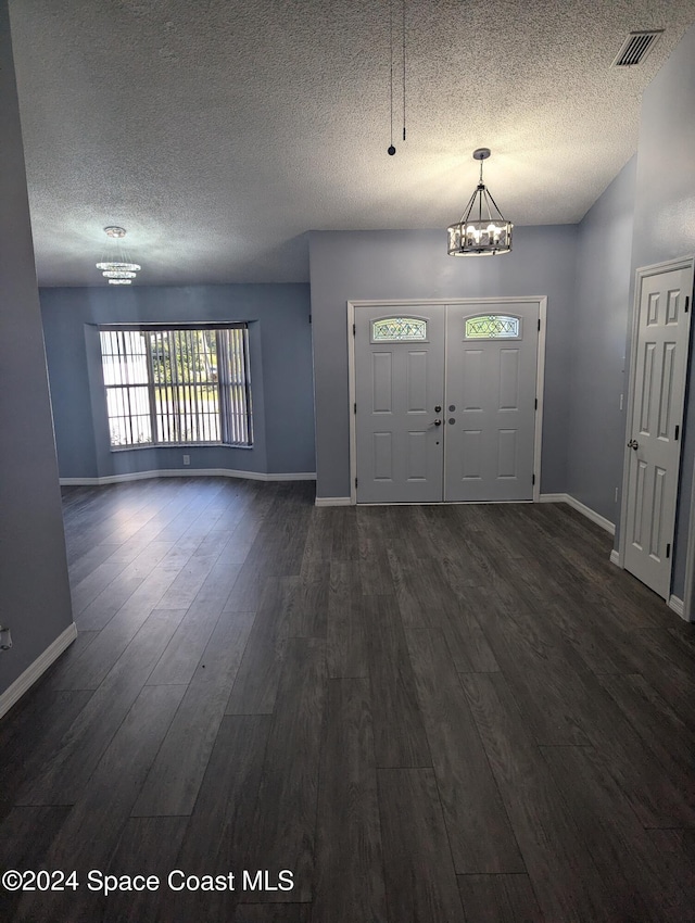 entryway with a chandelier, dark wood-type flooring, and a textured ceiling