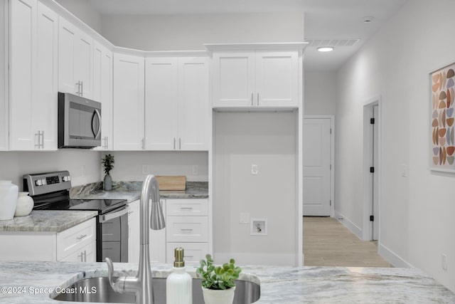 kitchen with white cabinets, appliances with stainless steel finishes, light hardwood / wood-style floors, and light stone counters