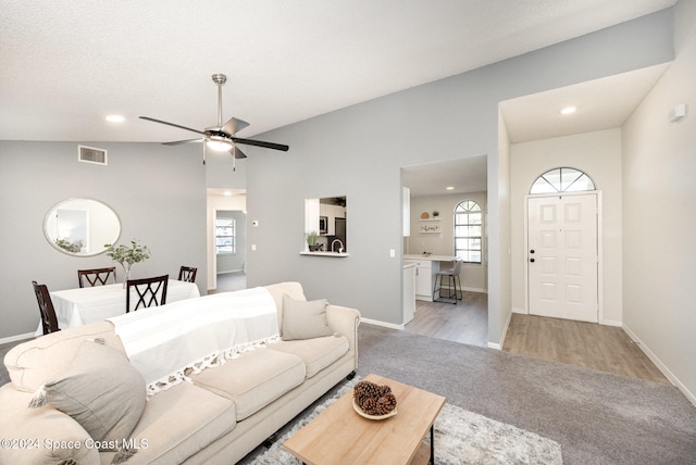 living room with ceiling fan, light hardwood / wood-style floors, a textured ceiling, and vaulted ceiling