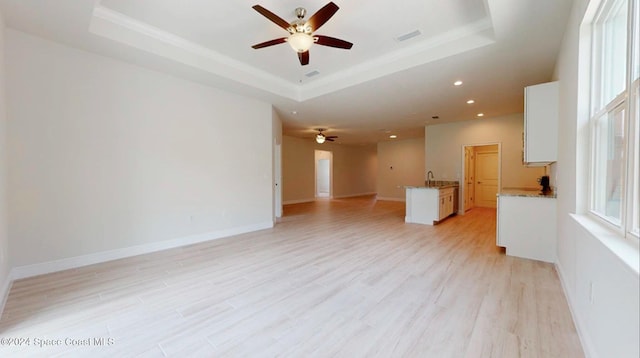 unfurnished living room featuring a tray ceiling, ceiling fan, light hardwood / wood-style flooring, and sink