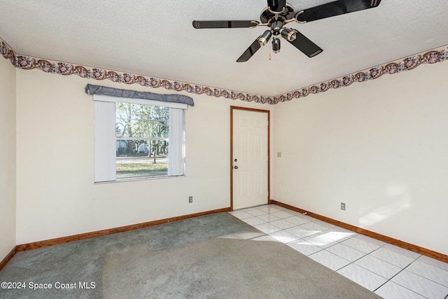 empty room featuring a textured ceiling, ceiling fan, and light tile patterned flooring