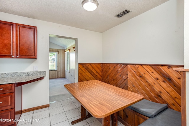 tiled dining space with a textured ceiling, vaulted ceiling, and wood walls