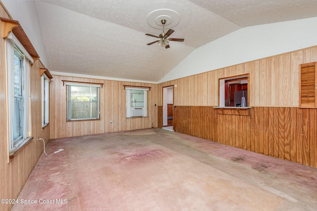 unfurnished room featuring a textured ceiling, wooden walls, and lofted ceiling