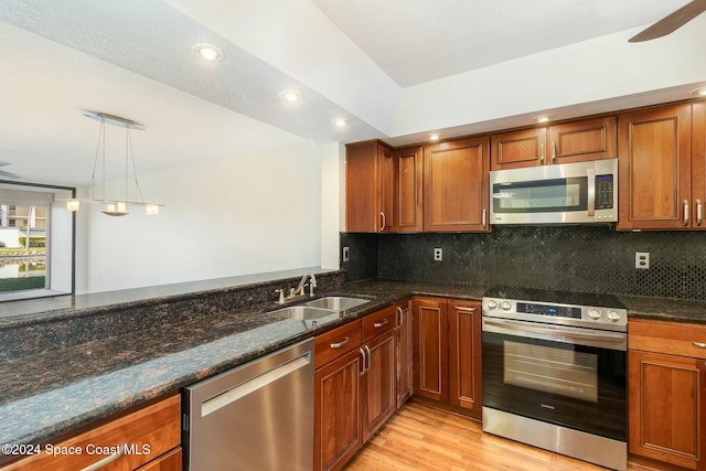 kitchen featuring sink, hanging light fixtures, light hardwood / wood-style flooring, backsplash, and appliances with stainless steel finishes