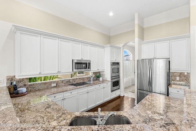 kitchen featuring backsplash, white cabinets, sink, light stone countertops, and appliances with stainless steel finishes