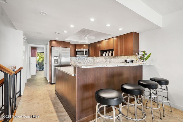 kitchen with ceiling fan, light stone counters, kitchen peninsula, a breakfast bar area, and appliances with stainless steel finishes