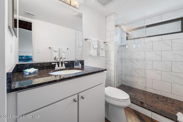 bathroom featuring hardwood / wood-style floors, vanity, a tile shower, and toilet