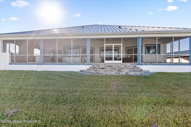 back of house with metal roof, a sunroom, a lawn, and a standing seam roof