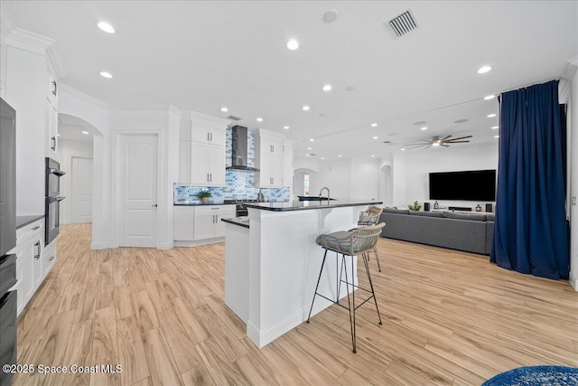 kitchen featuring visible vents, dark countertops, arched walkways, wall chimney exhaust hood, and white cabinets