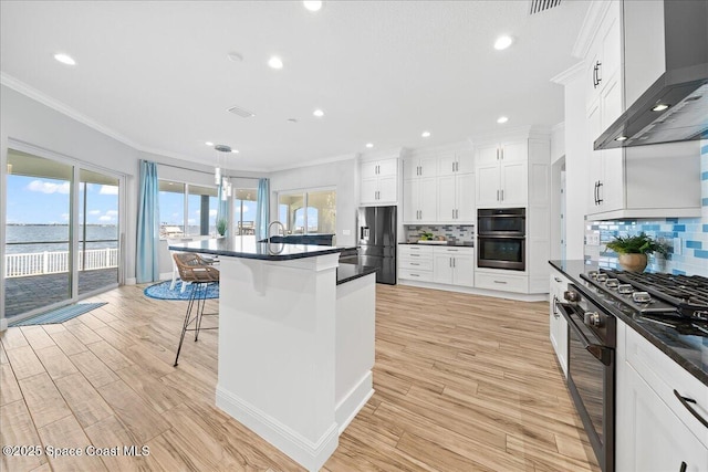 kitchen featuring black appliances, a kitchen breakfast bar, dark countertops, crown molding, and wall chimney range hood