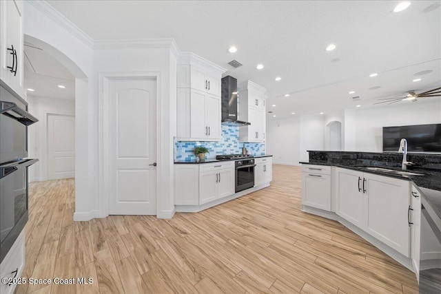 kitchen featuring arched walkways, a sink, stainless steel appliances, white cabinets, and wall chimney exhaust hood