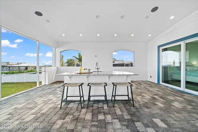 kitchen featuring brick floor, light stone countertops, recessed lighting, and a sink